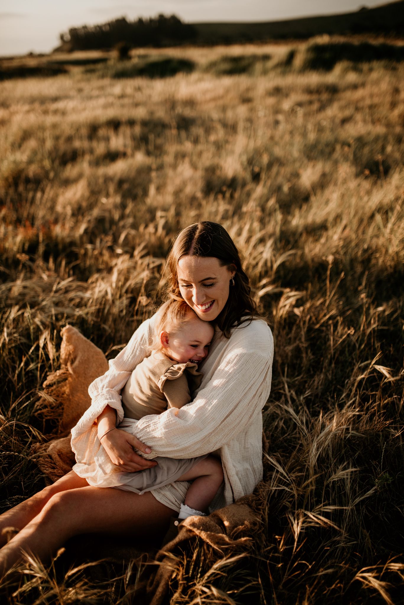 Tender moment captured in a sun-drenched field as two people embrace in matching white dresses.