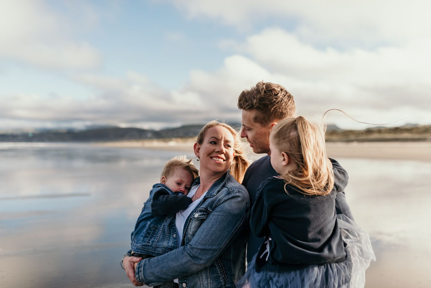 Candid family portrait at the beach with mountains and reflective water in the background.