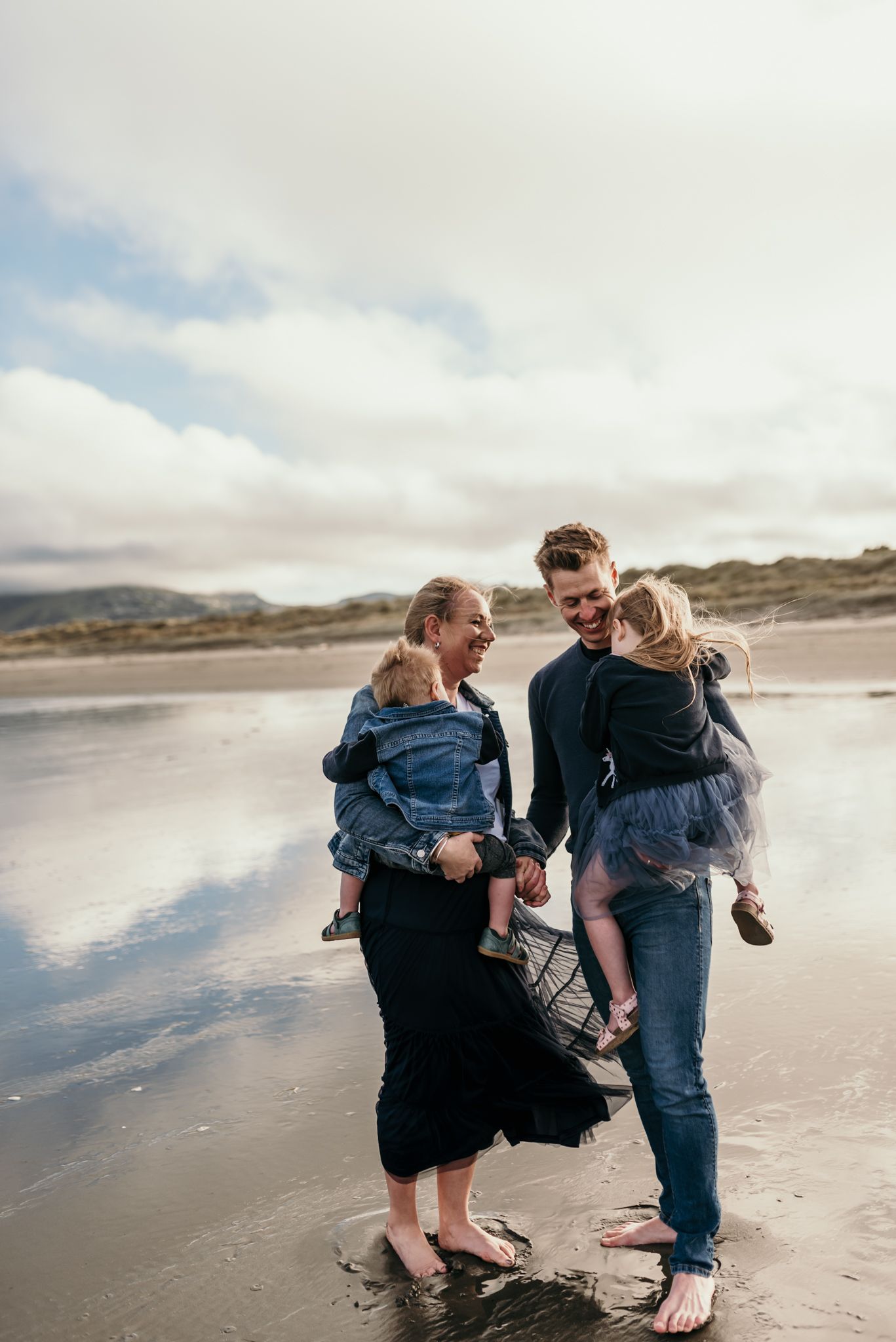 Intimate family portrait on a beach with reflective water and cloudy skies.