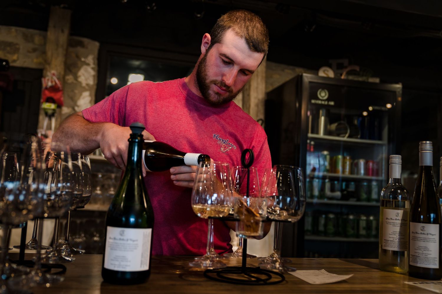 Bar scene showing wine glasses being filled in dimly lit setting.