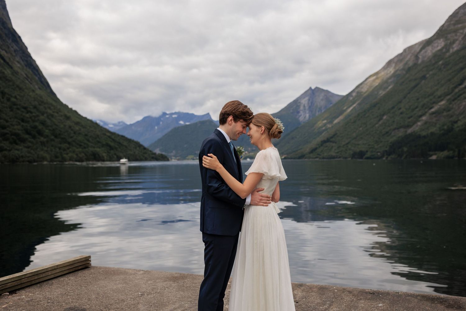 A romantic moment between a couple by a tranquil mountain lake with dramatic peaks in the background.