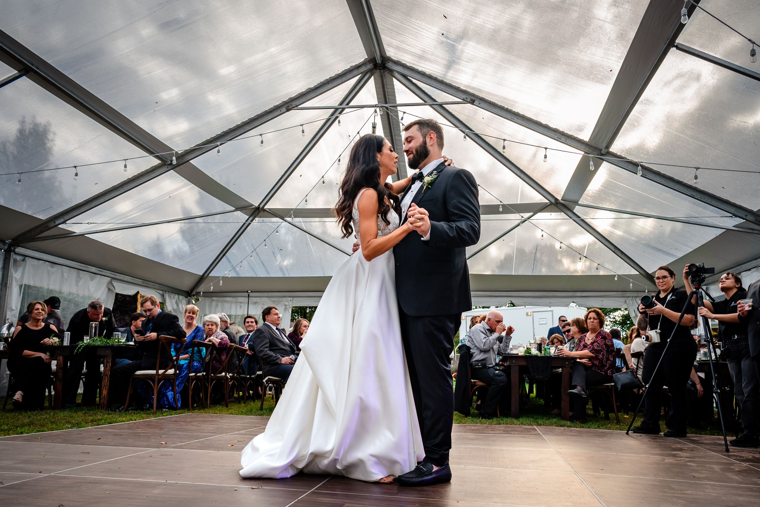First dance under clear tent with guests watching at wedding reception.