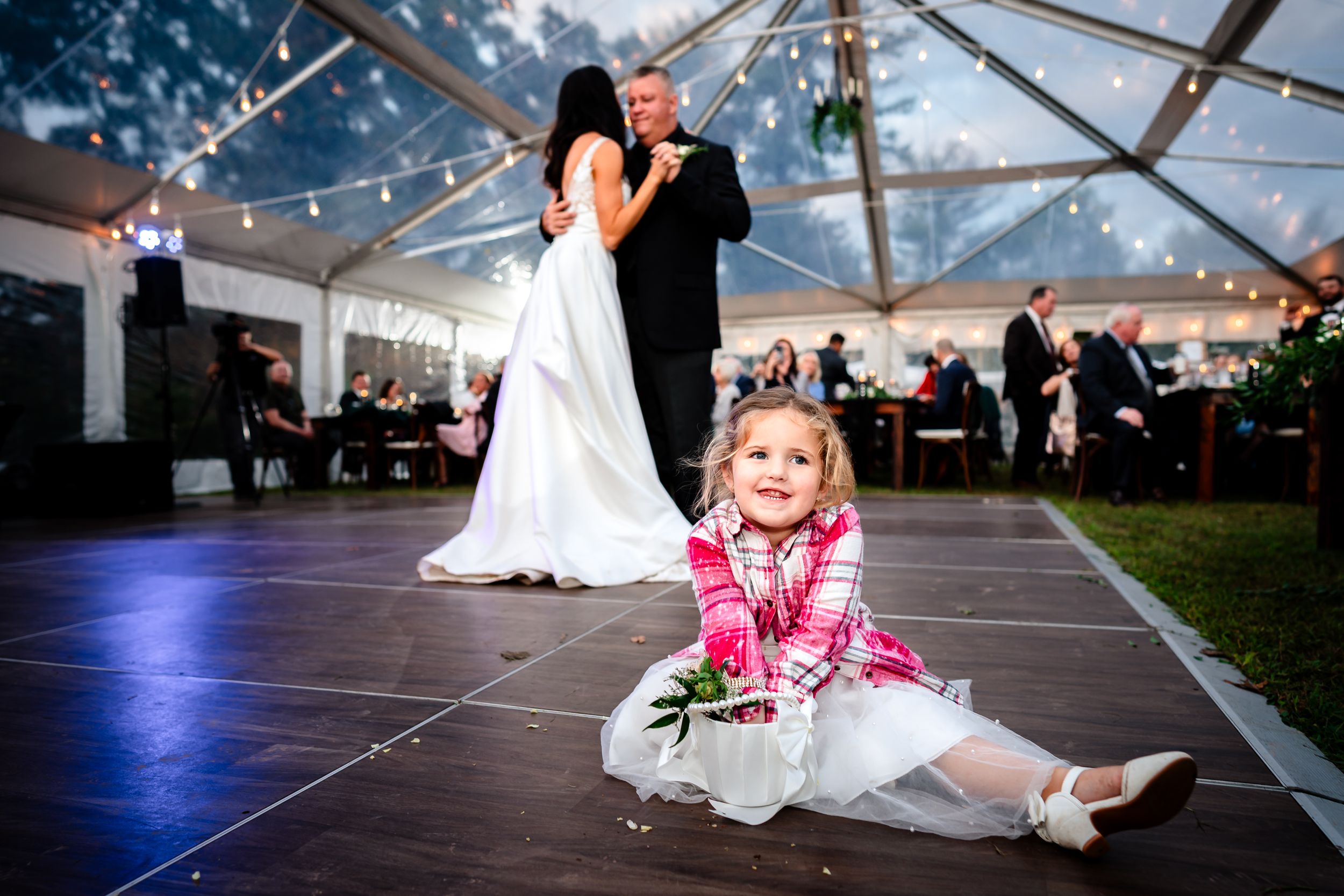 Clear tent wedding reception space decorated with string lights and dance floor.