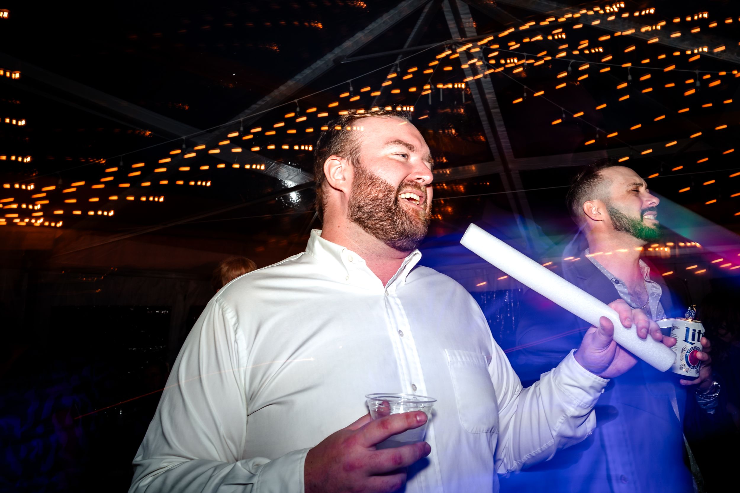 Party guests waving light-up foam sticks on a dark dance floor with string lights overhead.