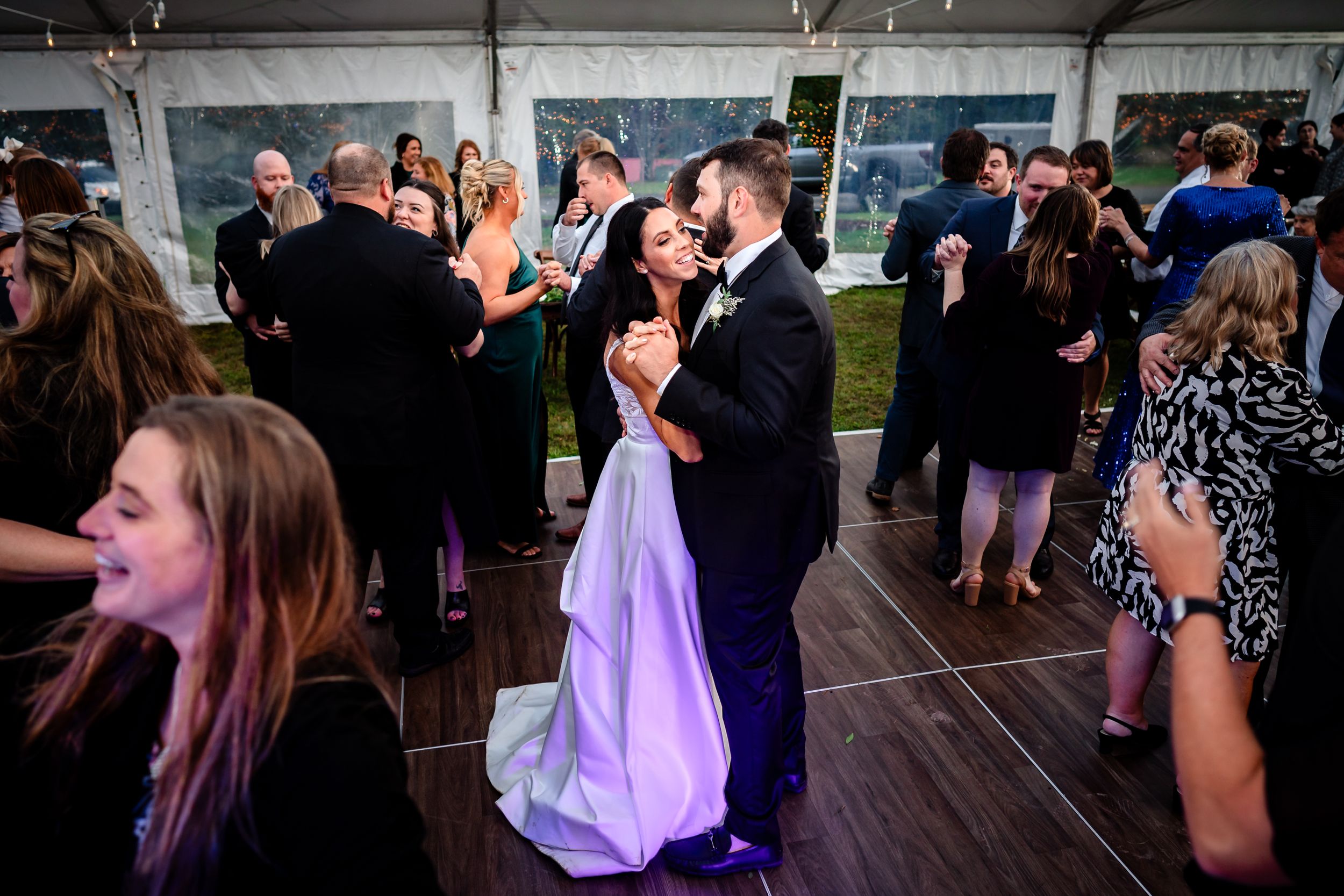 Wedding guests dancing and celebrating on a crowded dance floor at an evening reception.