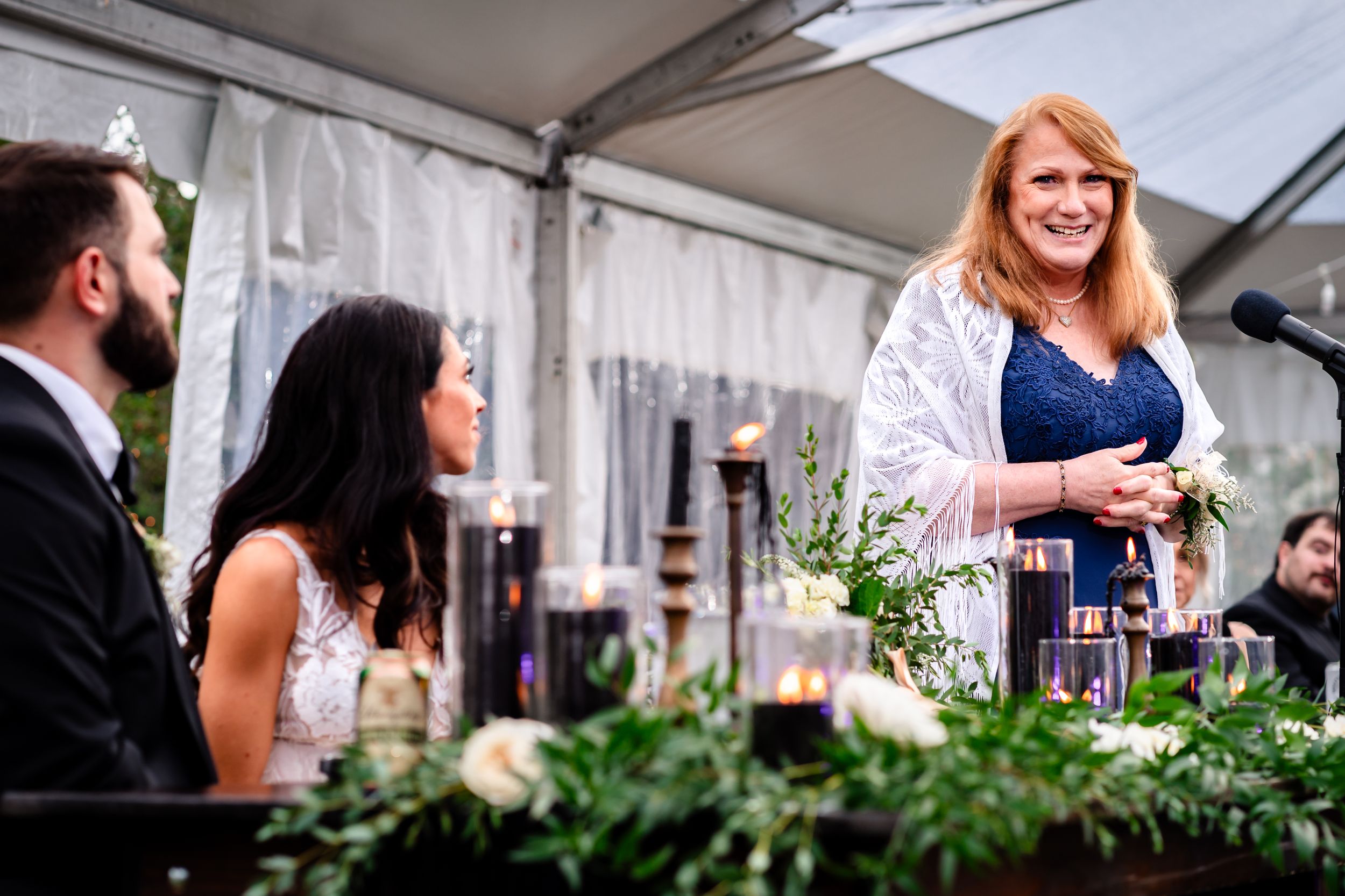 Wedding reception guests seated under a white tent with elegant floral decorations.