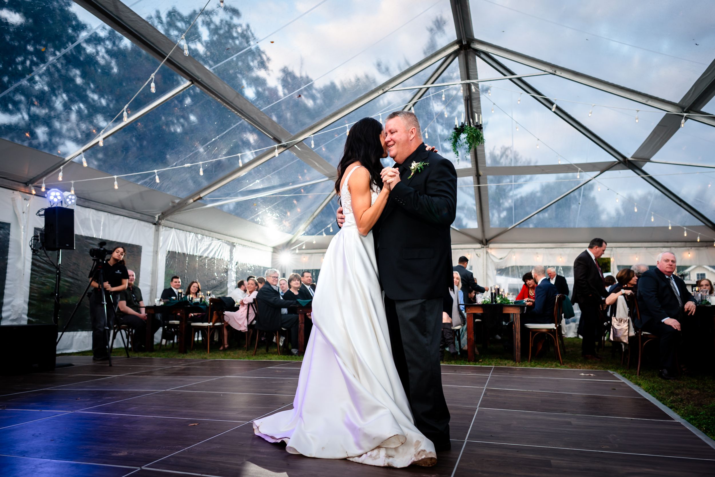 Wedding celebration inside clear tent venue with dancing and festive atmosphere.