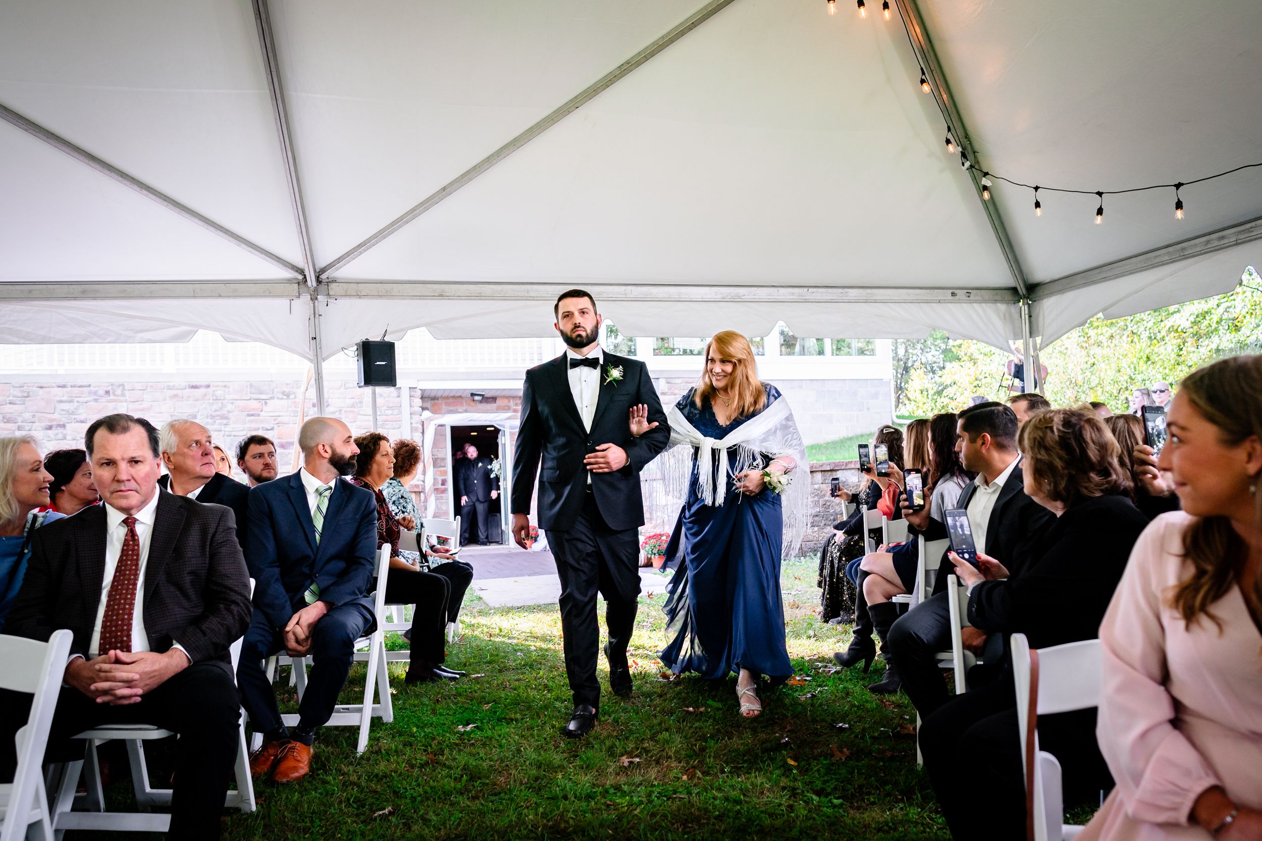 Wedding ceremony processional under white tent with guests seated on either side of aisle.