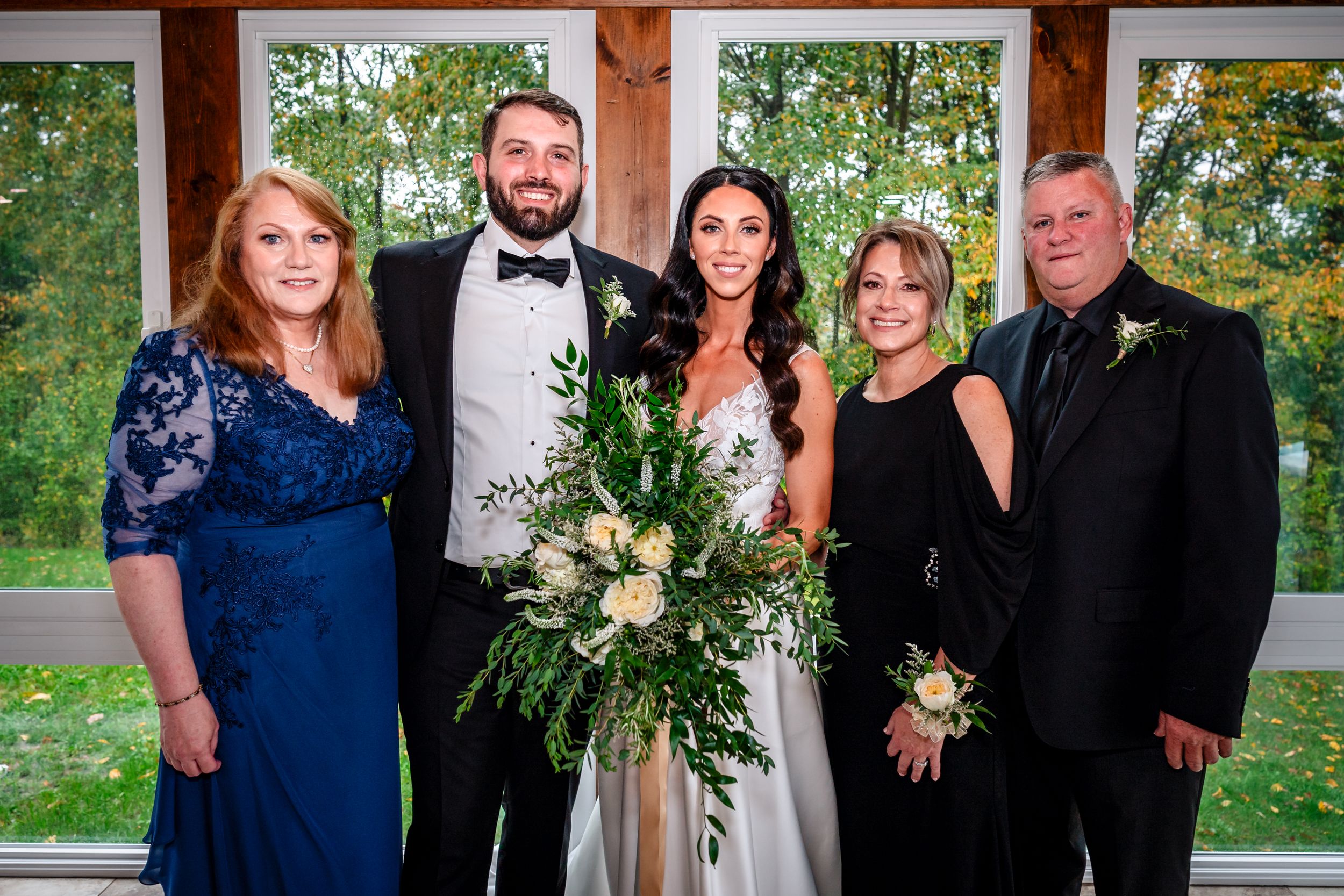 Wedding party and family members pose for formal group photo in rustic venue.