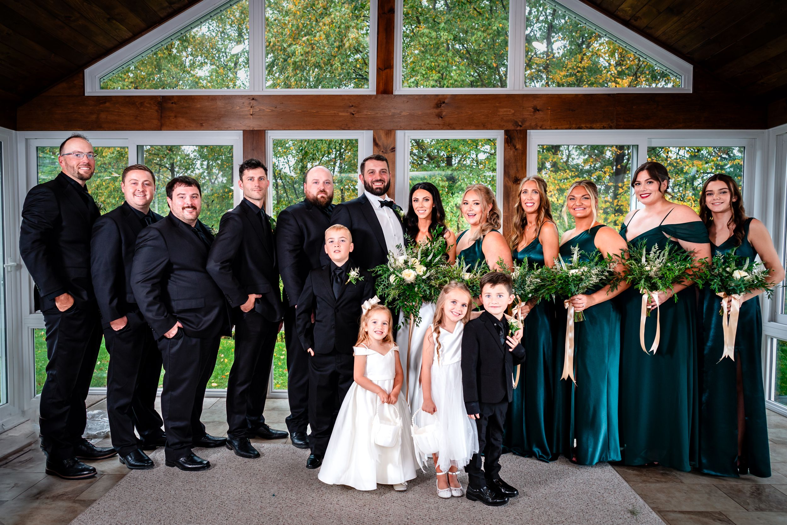 Complete wedding party poses together in formal attire with emerald dresses and black suits.