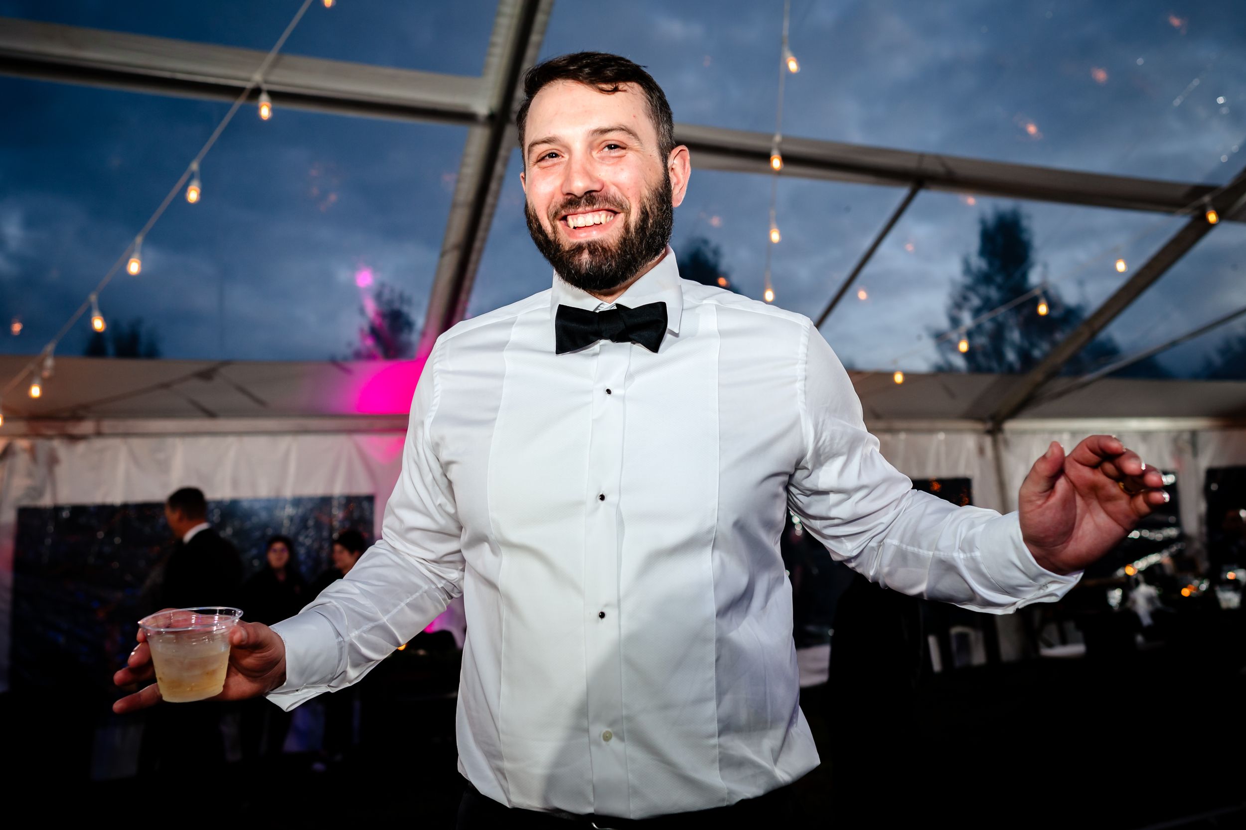 Wedding reception guests in formal attire dancing and smiling under string lights.