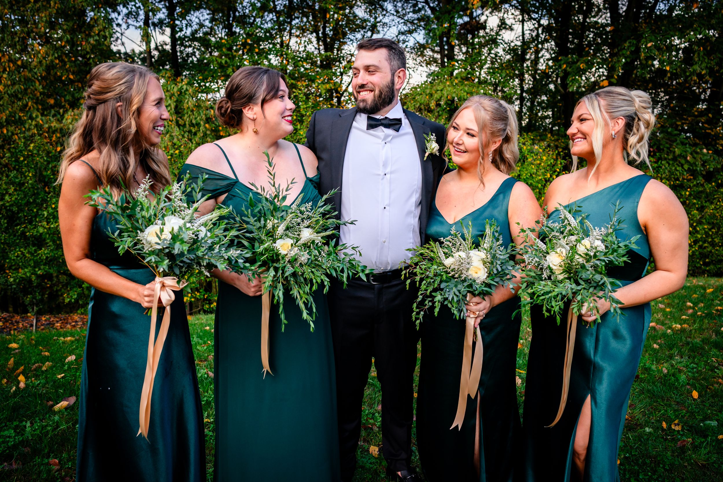 Bridal party in emerald green dresses poses together outdoors.