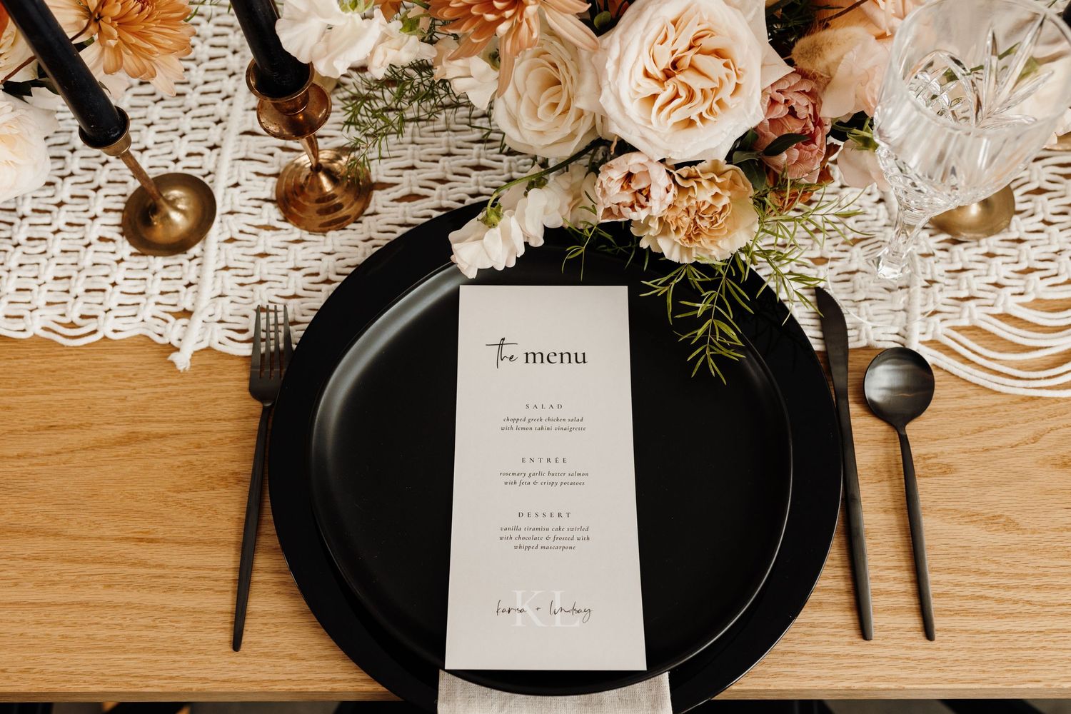 Elegant place setting with black plate, menu card and floral decorations on wooden table with lace details.