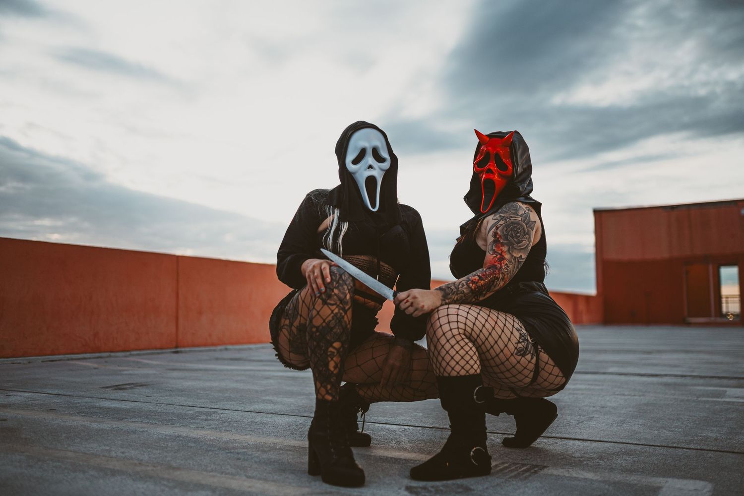 Two figures in Halloween costumes pose on a rooftop against a moody cloudy sky.
