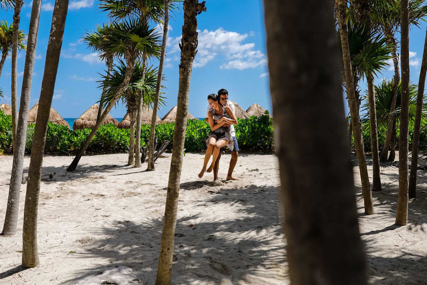 Couple running playfully through palm trees on a tropical beach.