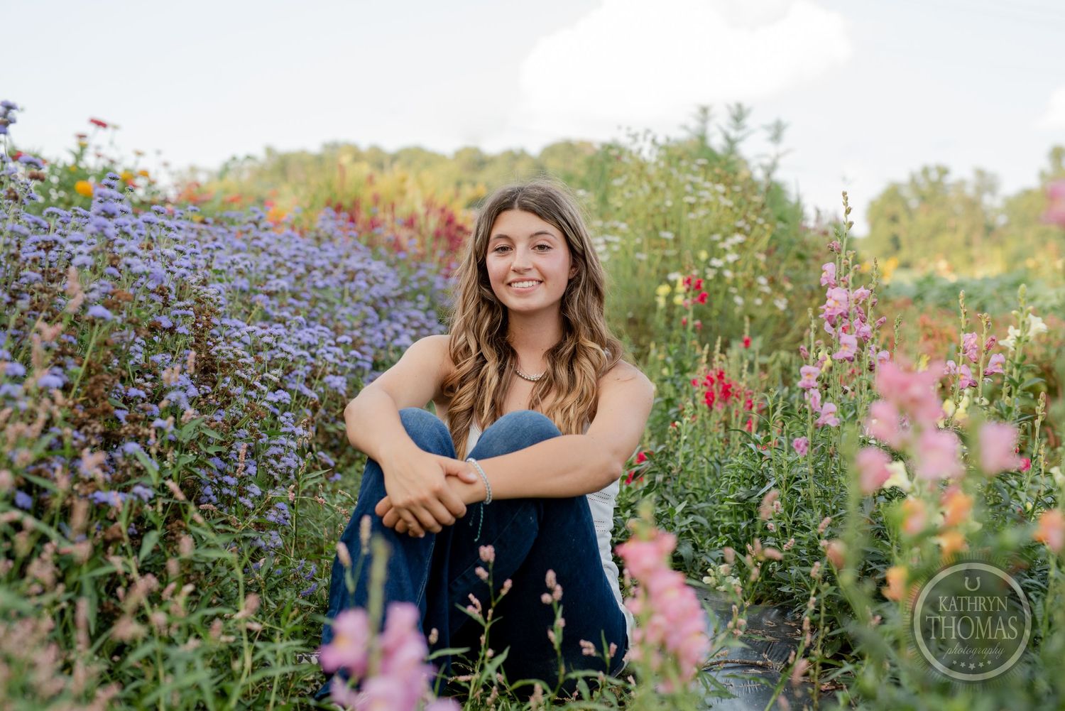 Person in blue dress sitting among purple and pink wildflowers in summer garden.
