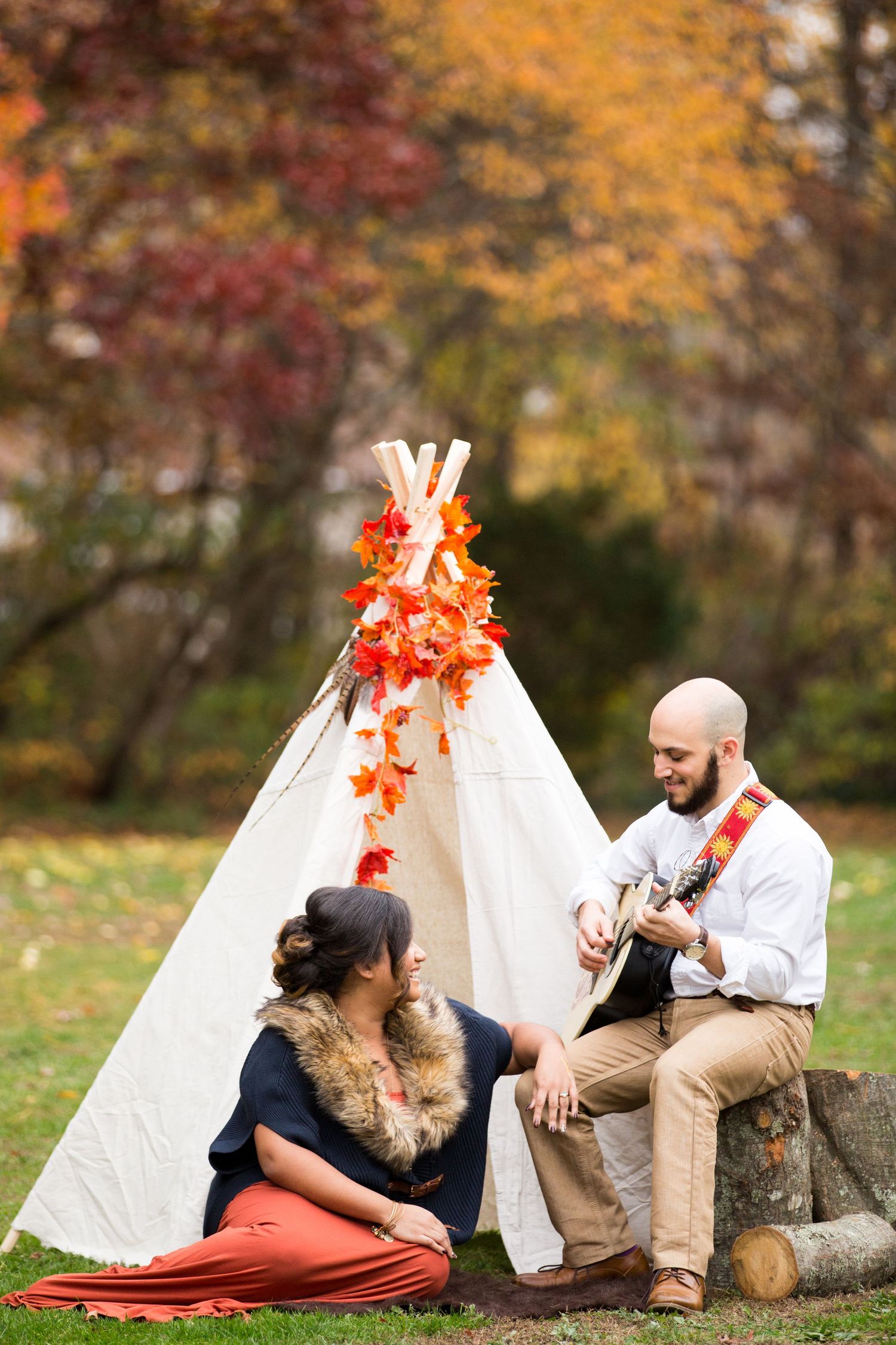 A cozy fall scene with a decorated teepee and acoustic guitar in autumn foliage.