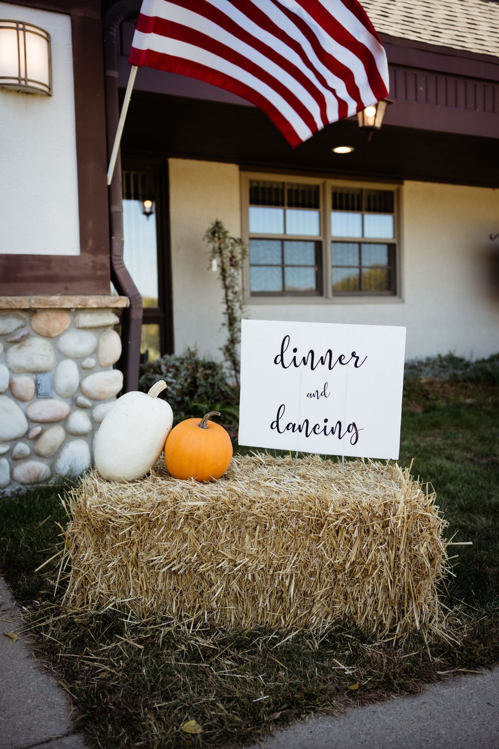 Fall wedding decor with hay bale, pumpkins and American flag outside rustic venue.