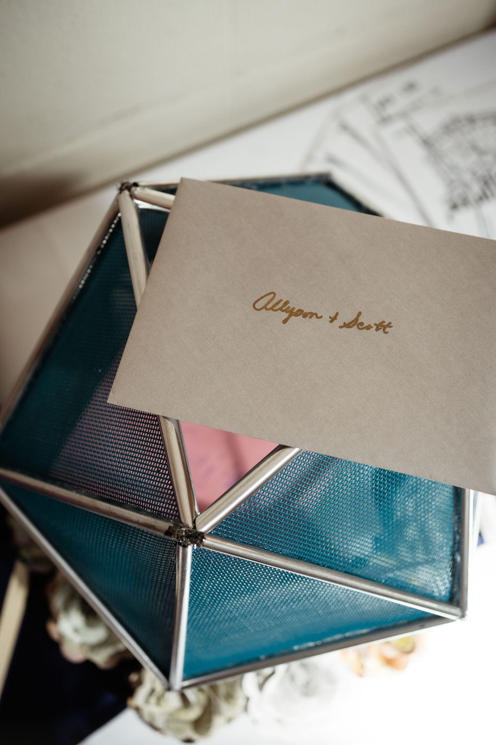 Elegant wedding invitation with gold lettering on beige paper against teal background.