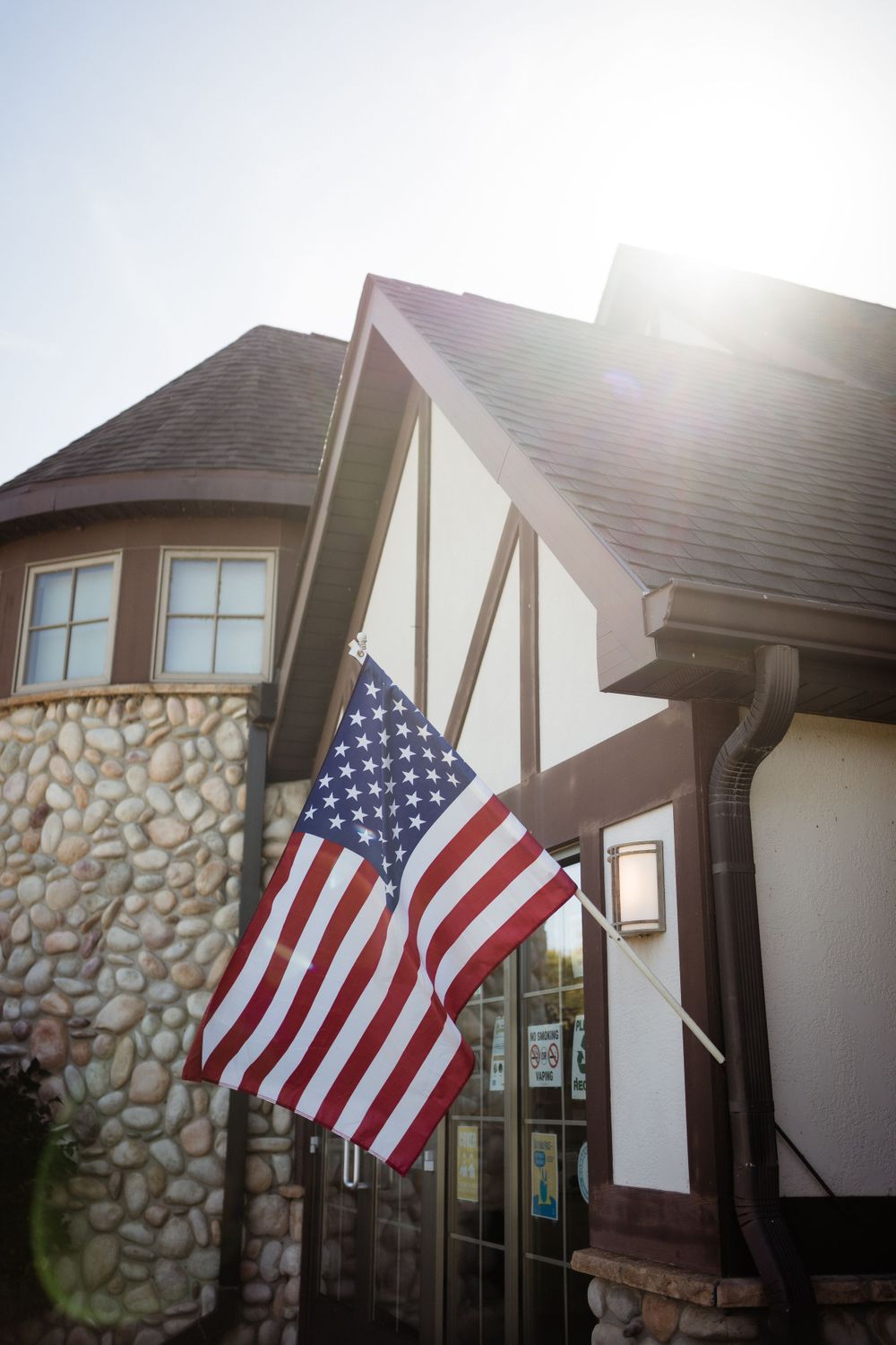 American flag displayed on a stone and stucco home exterior in bright sunlight.