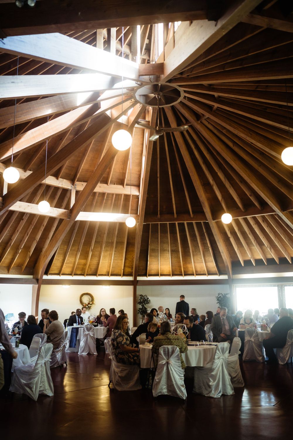 Wedding reception venue with dramatic wooden beam ceiling and elegant white table settings.