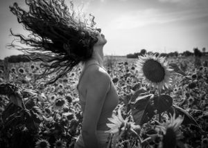 Artistic black and white portrait amidst towering sunflowers with dramatic sky.