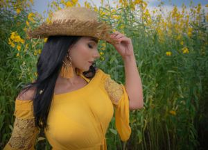 Someone in a yellow top poses artistically among tall sunflowers against blue sky.