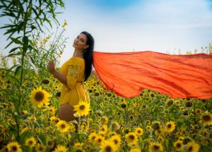 Orange fabric flows in the wind against a backdrop of towering sunflowers and blue sky.