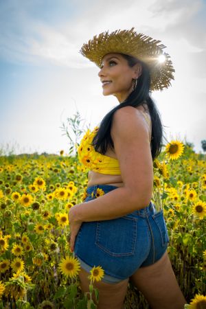 A sunflower field photoshoot featuring someone in denim and a straw hat surrounded by golden blooms.