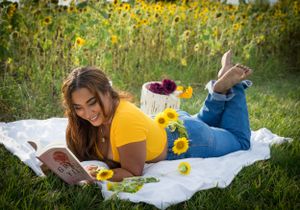 Someone relaxes on a white blanket in a sunflower field while reading a book.