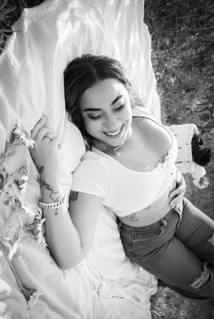 A black and white portrait photo shows someone lying on white fabric with soft, natural lighting.