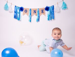 Blue and white birthday decorations with 'ONE' banner against white backdrop.