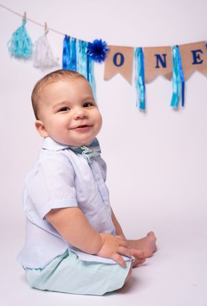 Baby sitting beneath blue birthday banner during first birthday photo session.
