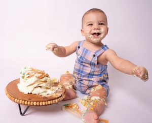 Baby in blue and white outfit enjoying messy cake smash photo session.