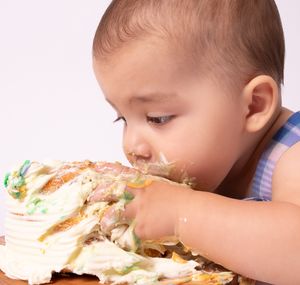 Close up of baby messily eating cake during first birthday celebration.