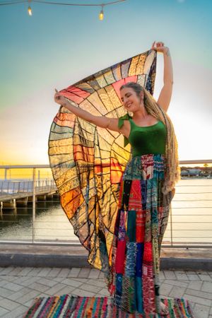 A colorful tie-dye butterfly wing cape flows gracefully during a sunset photoshoot on a rooftop.