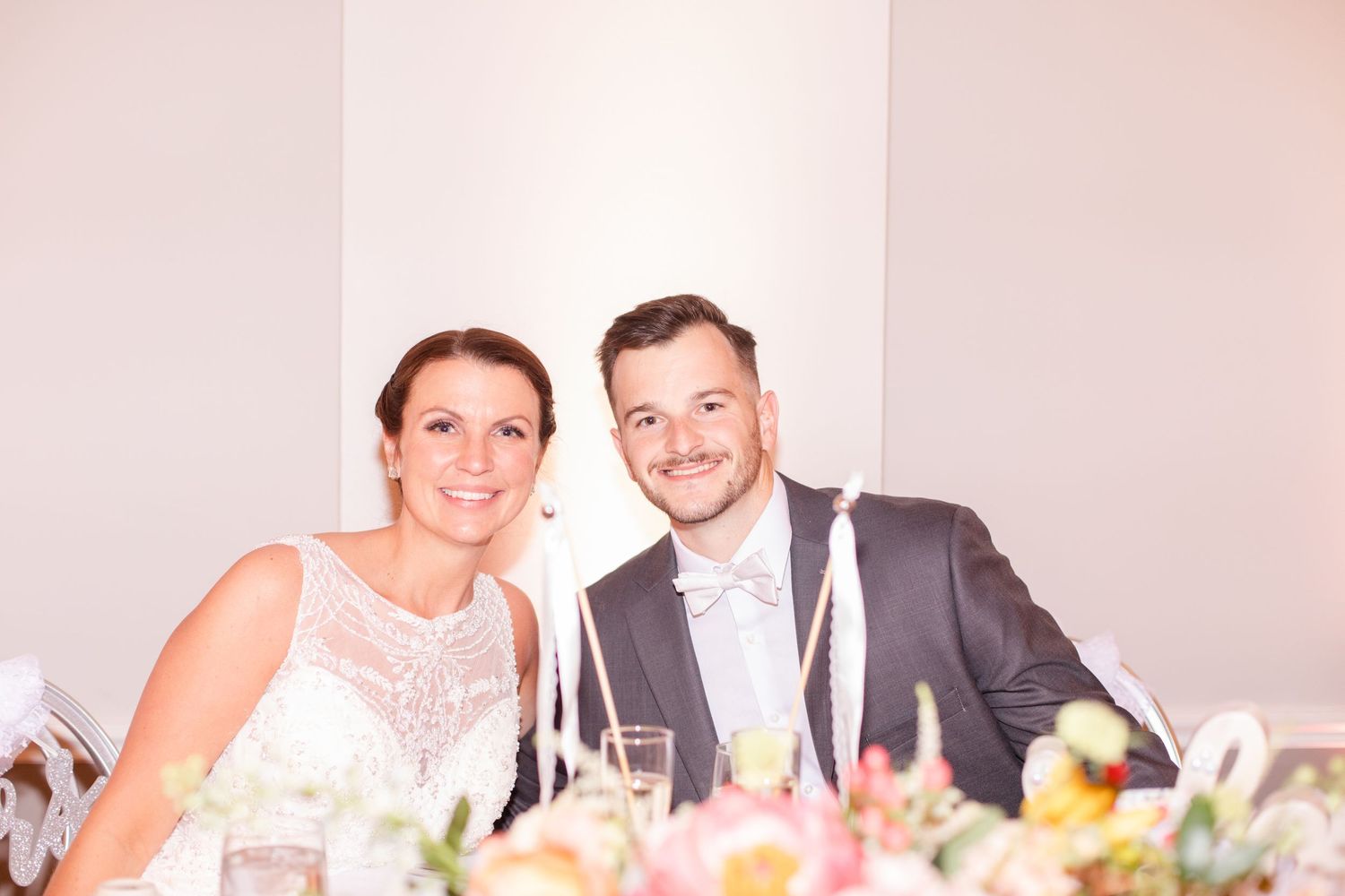 Formal wedding reception with guests dining at decorated tables in an elegant white room.