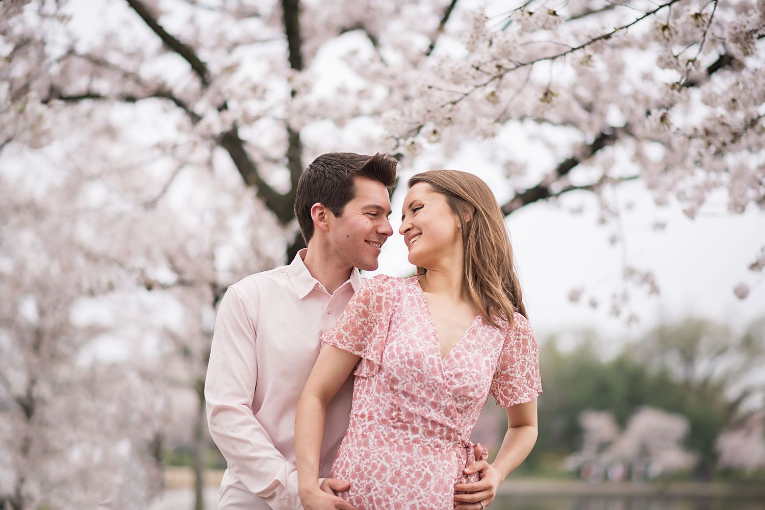 Couple in pastel outfits share intimate moment under blooming cherry blossom trees.