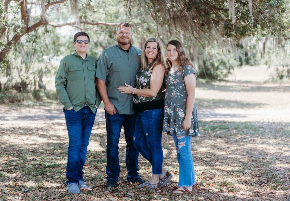 Casual outdoor family portrait taken under moss-draped trees.