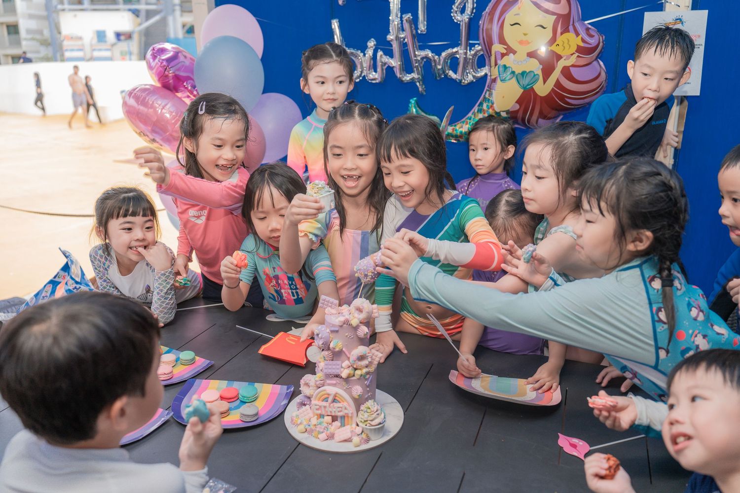 Children gathered around a birthday cake at a party with blue decorative background.