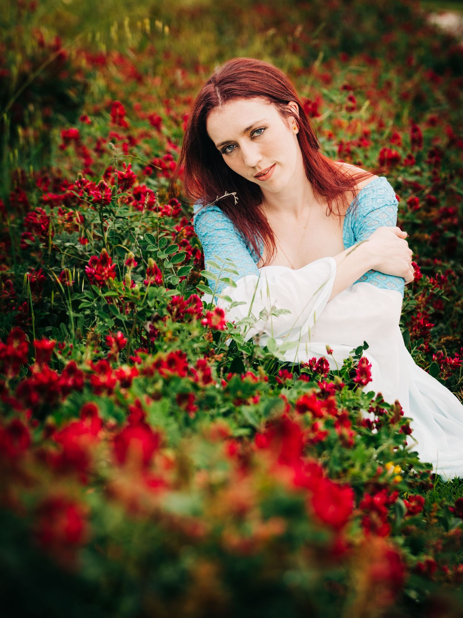 Dreamy portrait in garden with red flowers featuring ethereal white dress and romantic styling.
