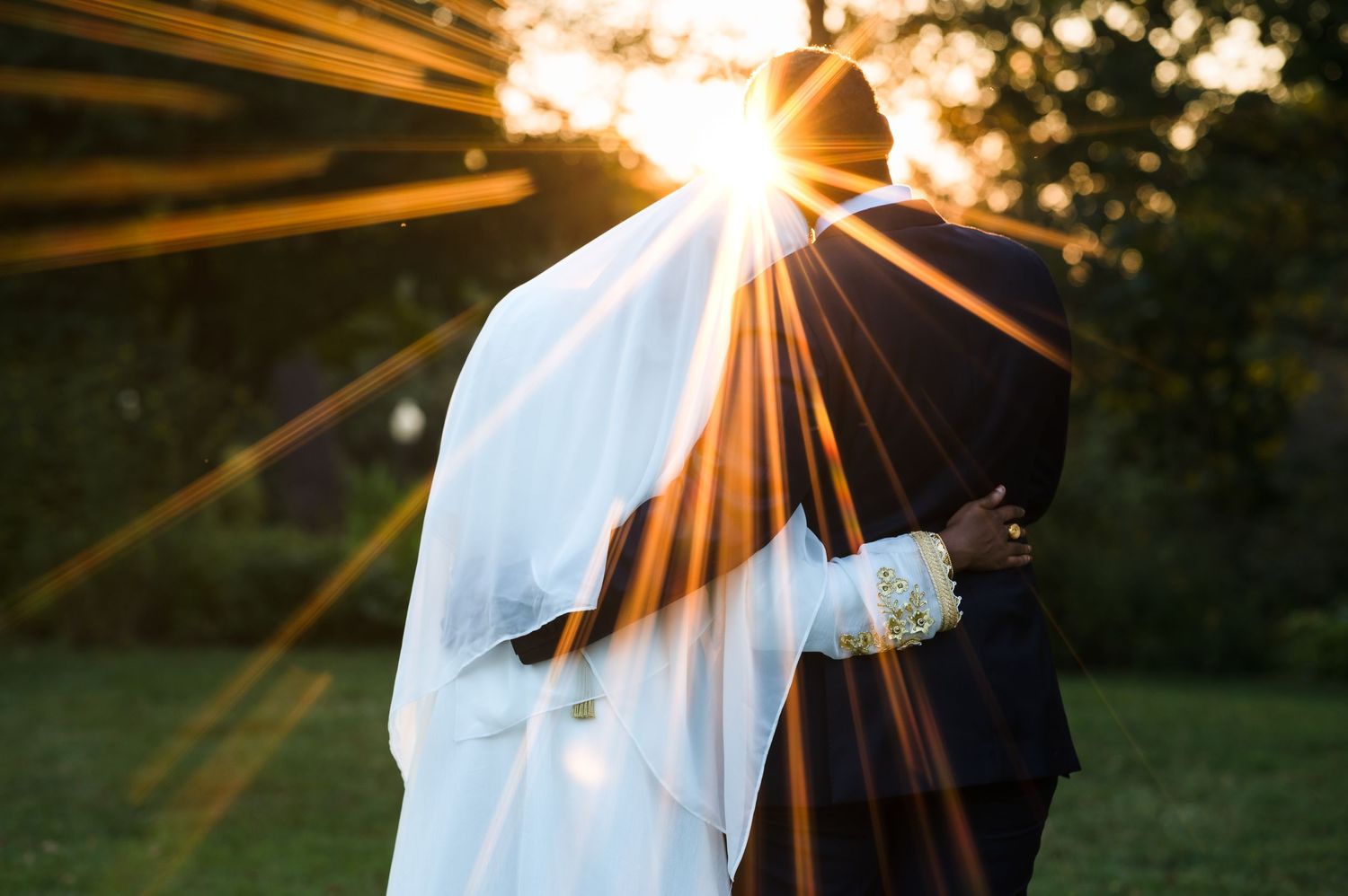 Silhouetted figures in formal attire with dramatic sunset rays bursting through.