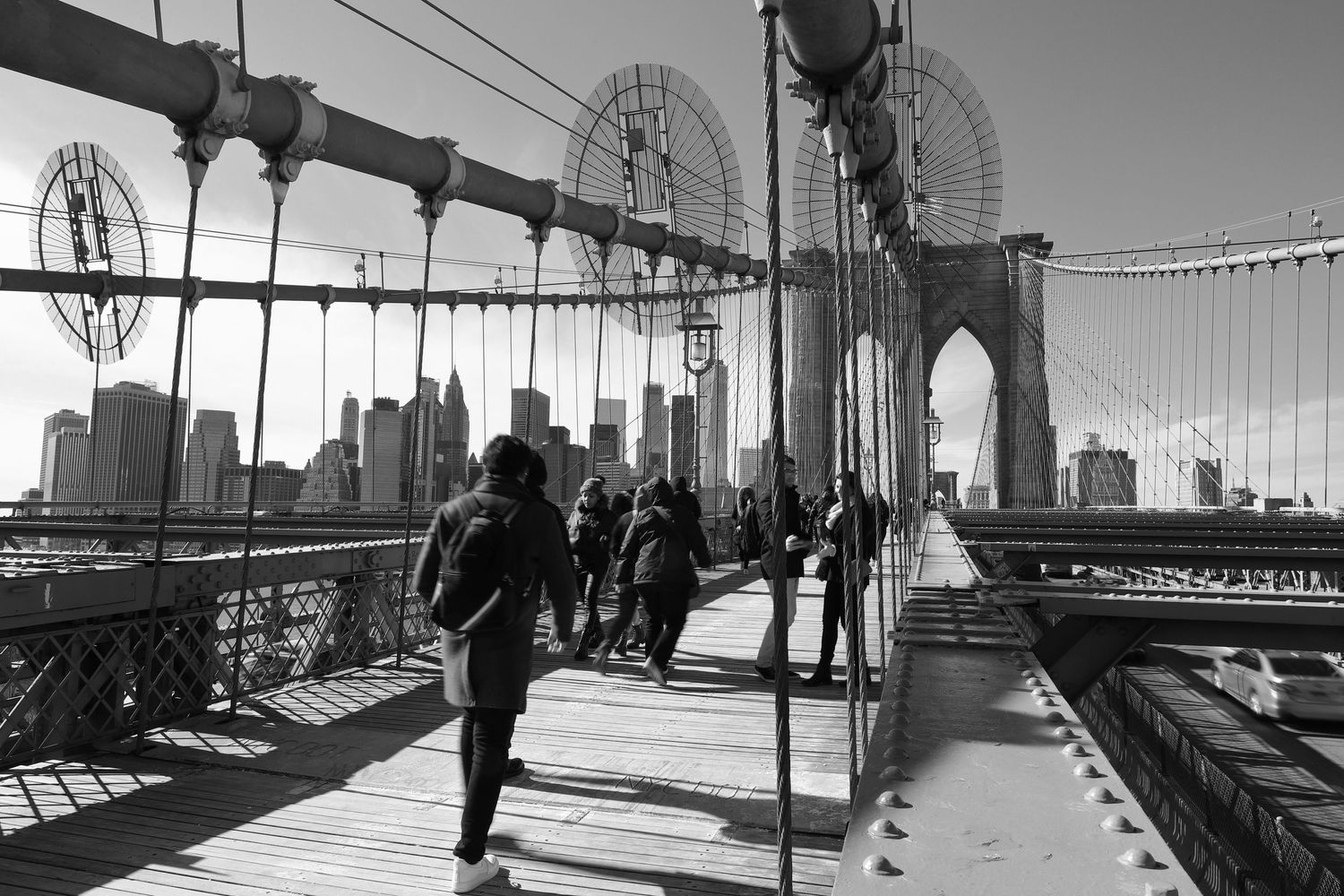 Pedestrians walking along the Brooklyn Bridge with iconic steel cables and arches.