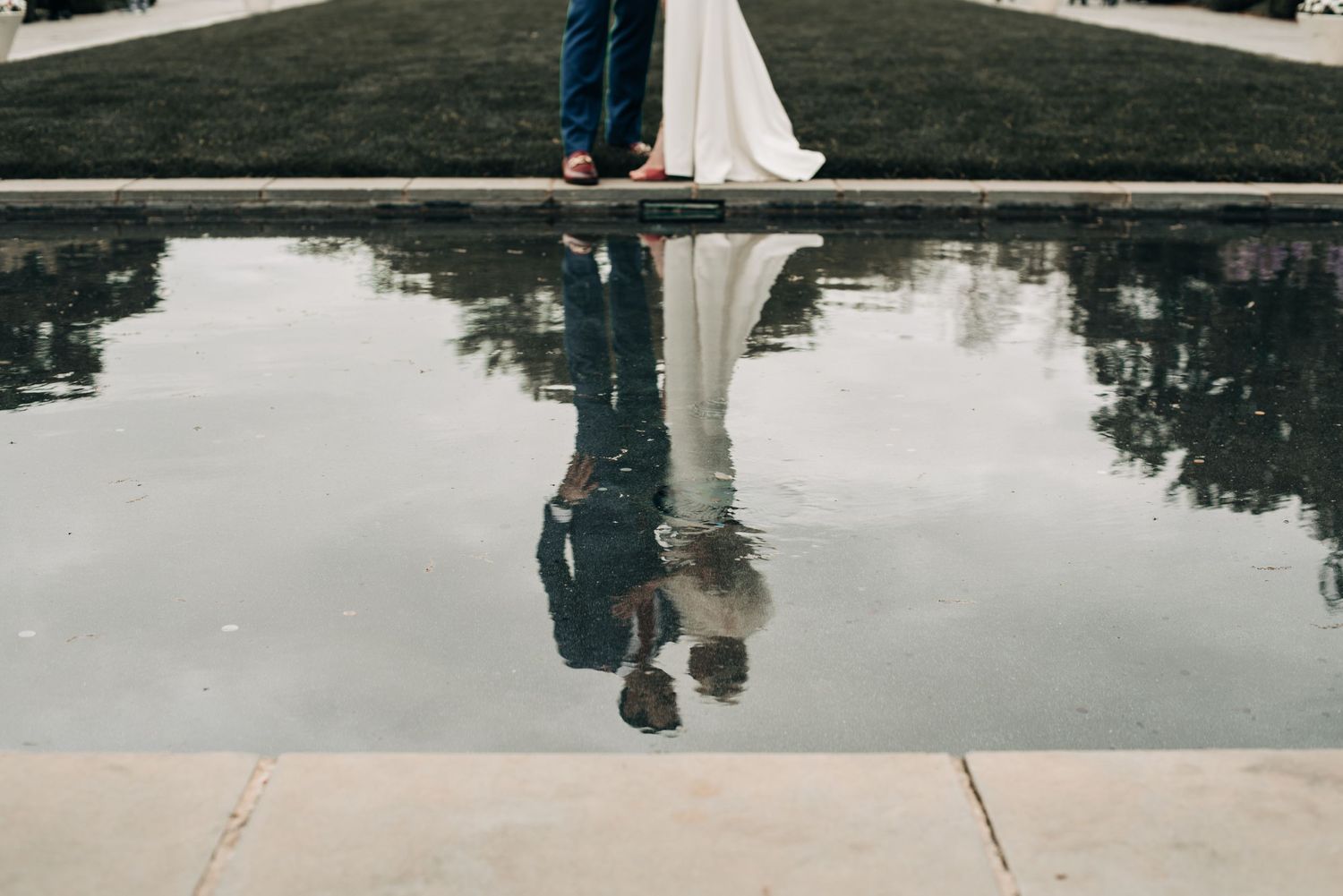 Wedding dress reflection in still water with feet visible at the edge of a pool.