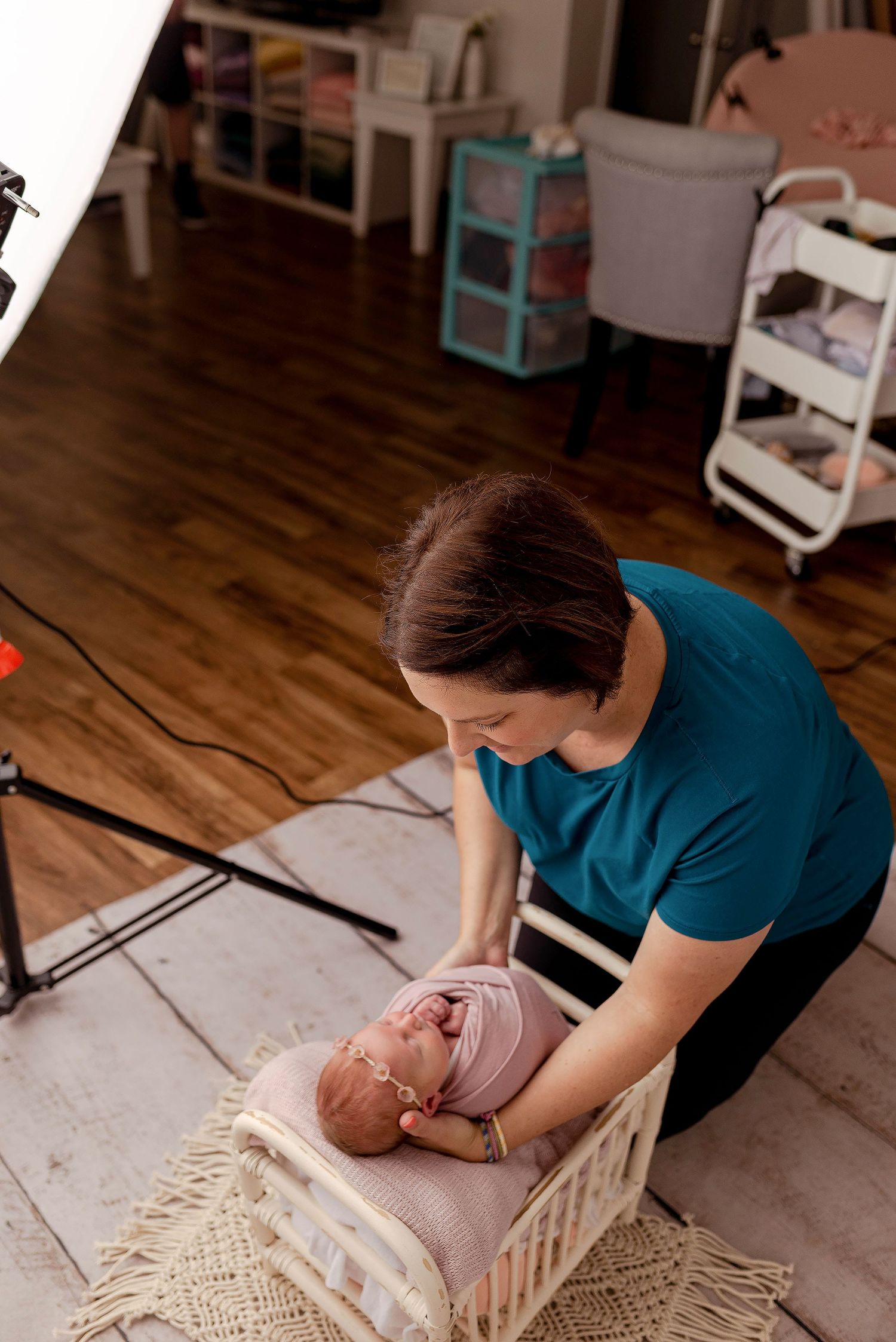 Professional newborn photographer carefully poses sleeping swaddled baby in tiny white crib in studio.