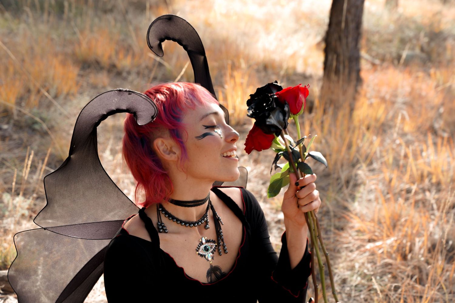 Fantasy-styled portrait with dark wings and red rose against autumn background.