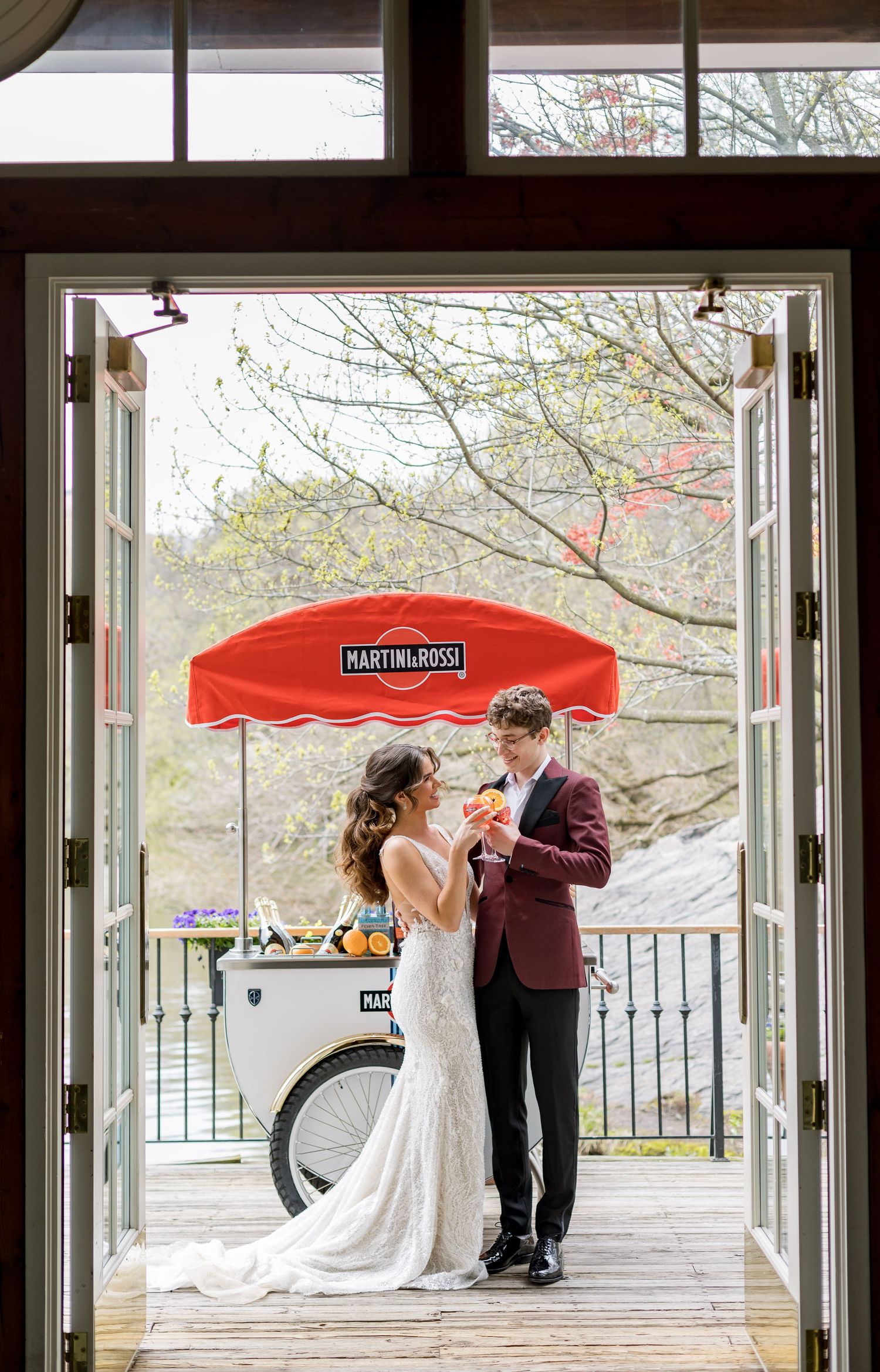 Wedding couple sharing a romantic moment under a red Martini & Rossi umbrella on a deck.