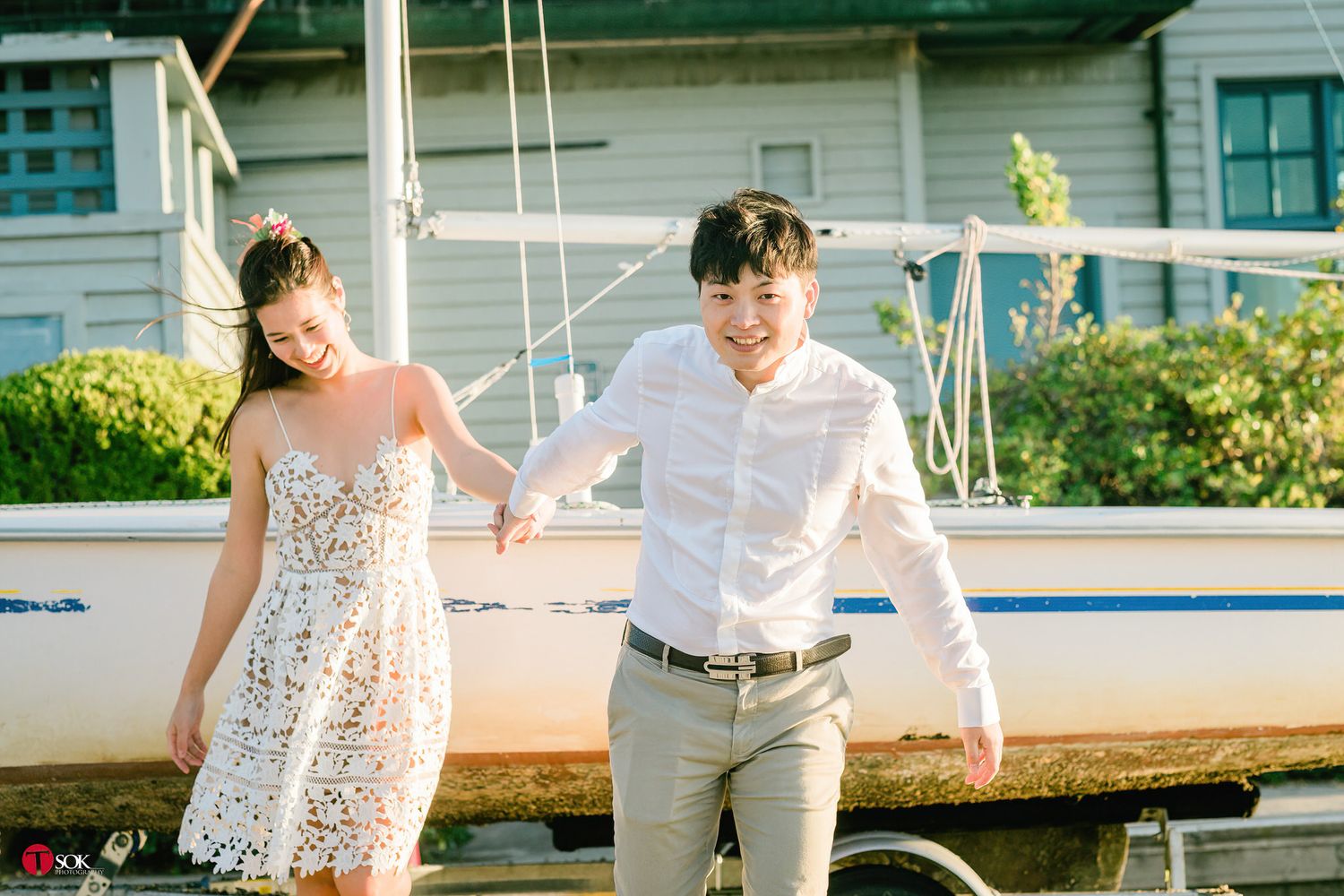 Couple strolling beside white sailboat on sunny day.