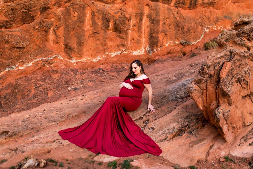 A flowing red maternity gown creates striking contrast against red rock canyon walls.