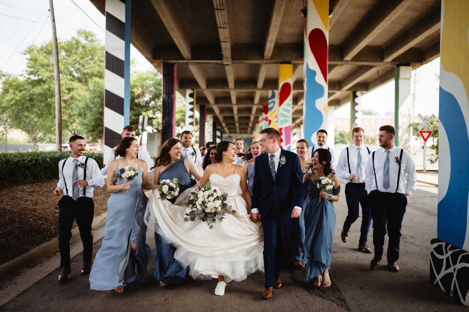 Wedding party walks and celebrates under a colorful urban underpass.